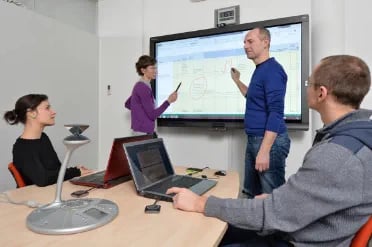 اجتماع فريق تفاعلي فيه مُقدِّم يستخدم SMART Board لتوضيح النقاط للزملاء المشاركين في غرفة مؤتمرات.